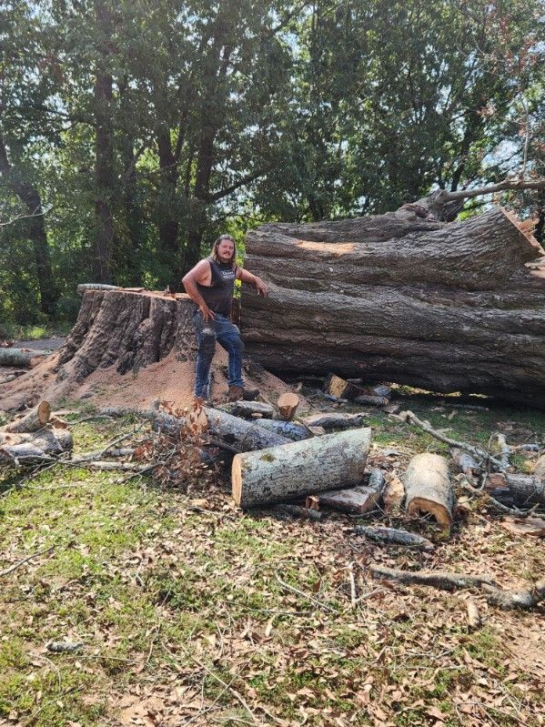 A man is standing next to a large log in a field.