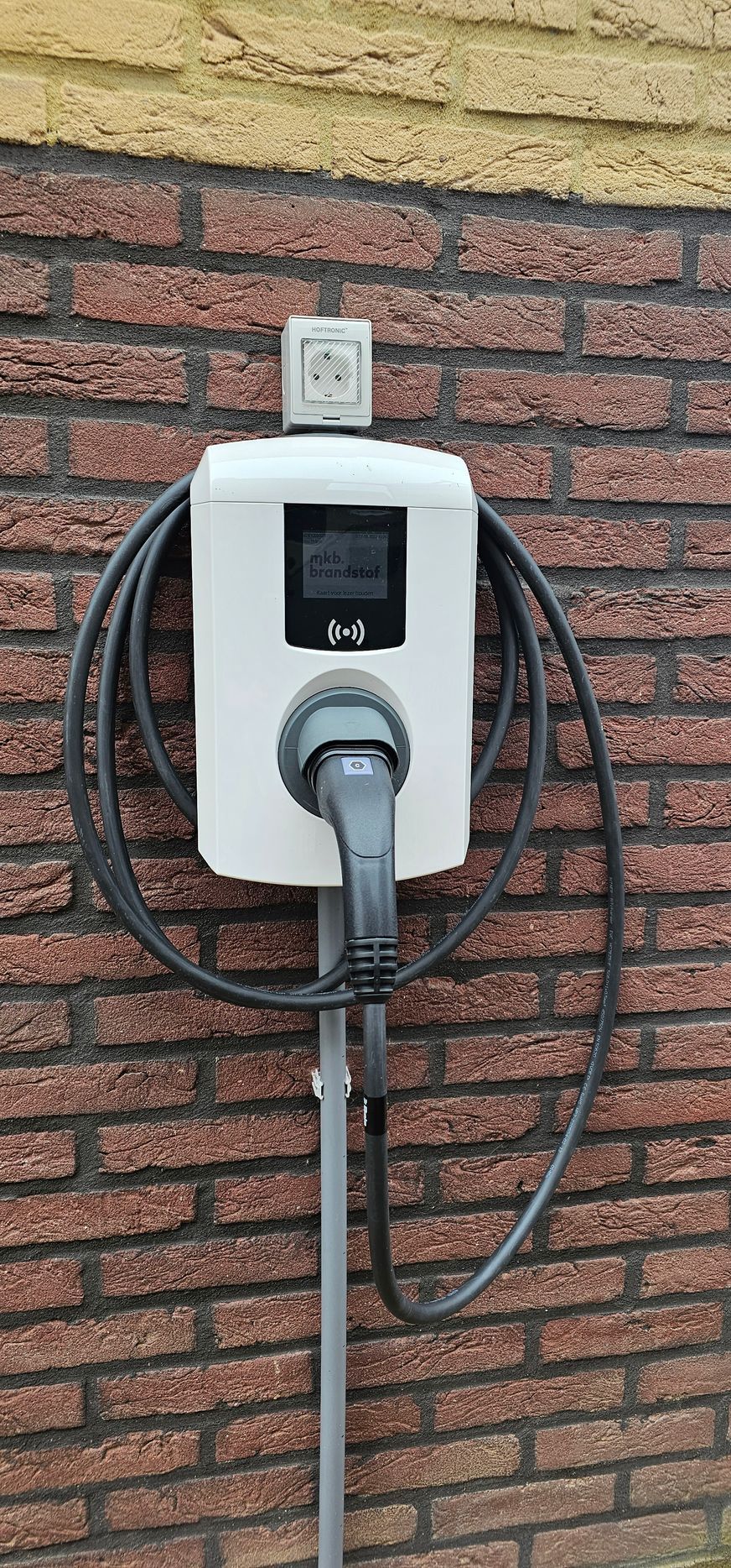 Een witte elektrische autolader is bevestigd aan een bakstenen muur.