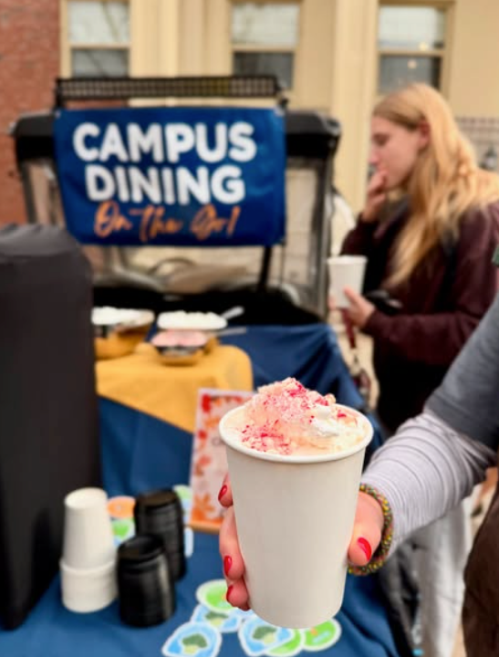 Person holding a cup with whipped cream at a campus dining stand. A sign reads 
