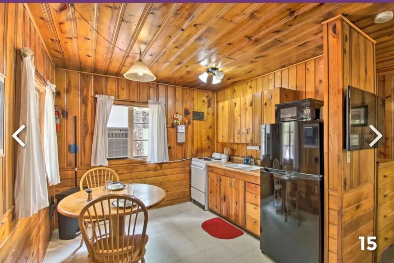 Cozy wood-paneled kitchen with round table, window curtains, stainless fridge, and cabinets
