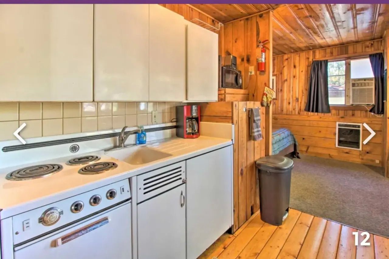 Compact wood-paneled kitchen with white stove, sink, cabinets, and a small living area beyond