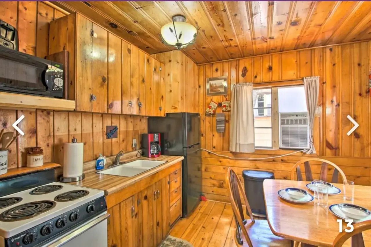Wood-paneled kitchen with stove, sink, table, and window air conditioner