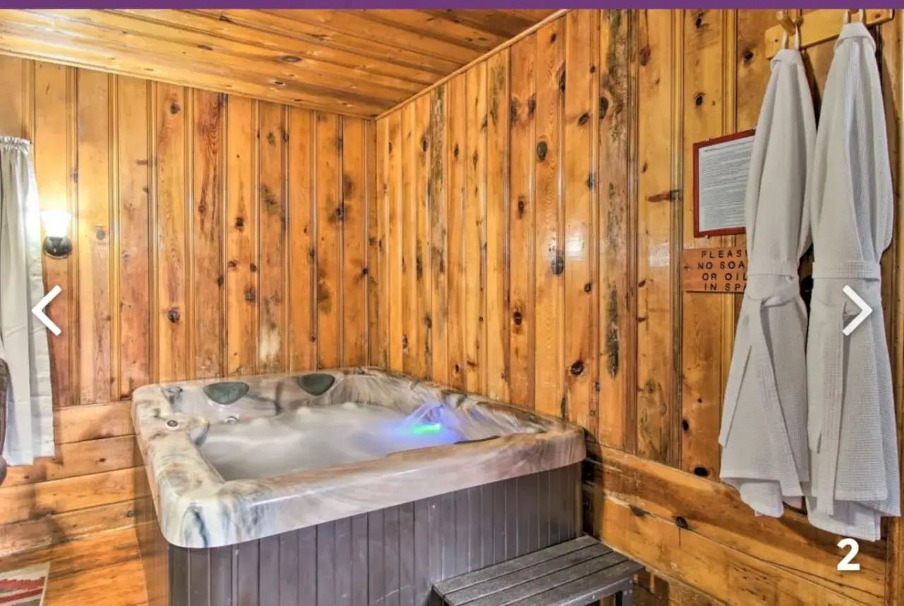 Wood-paneled hot tub room with a tiled spa, window light, and white robes hanging on the wall