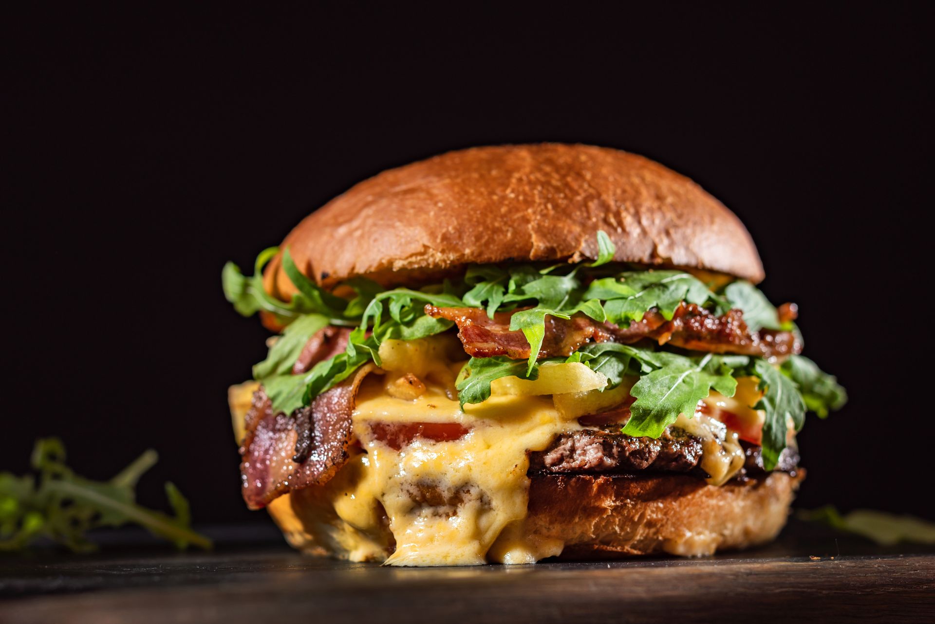 Juicy cheeseburger with melted cheese, lettuce, and bacon on a dark background
