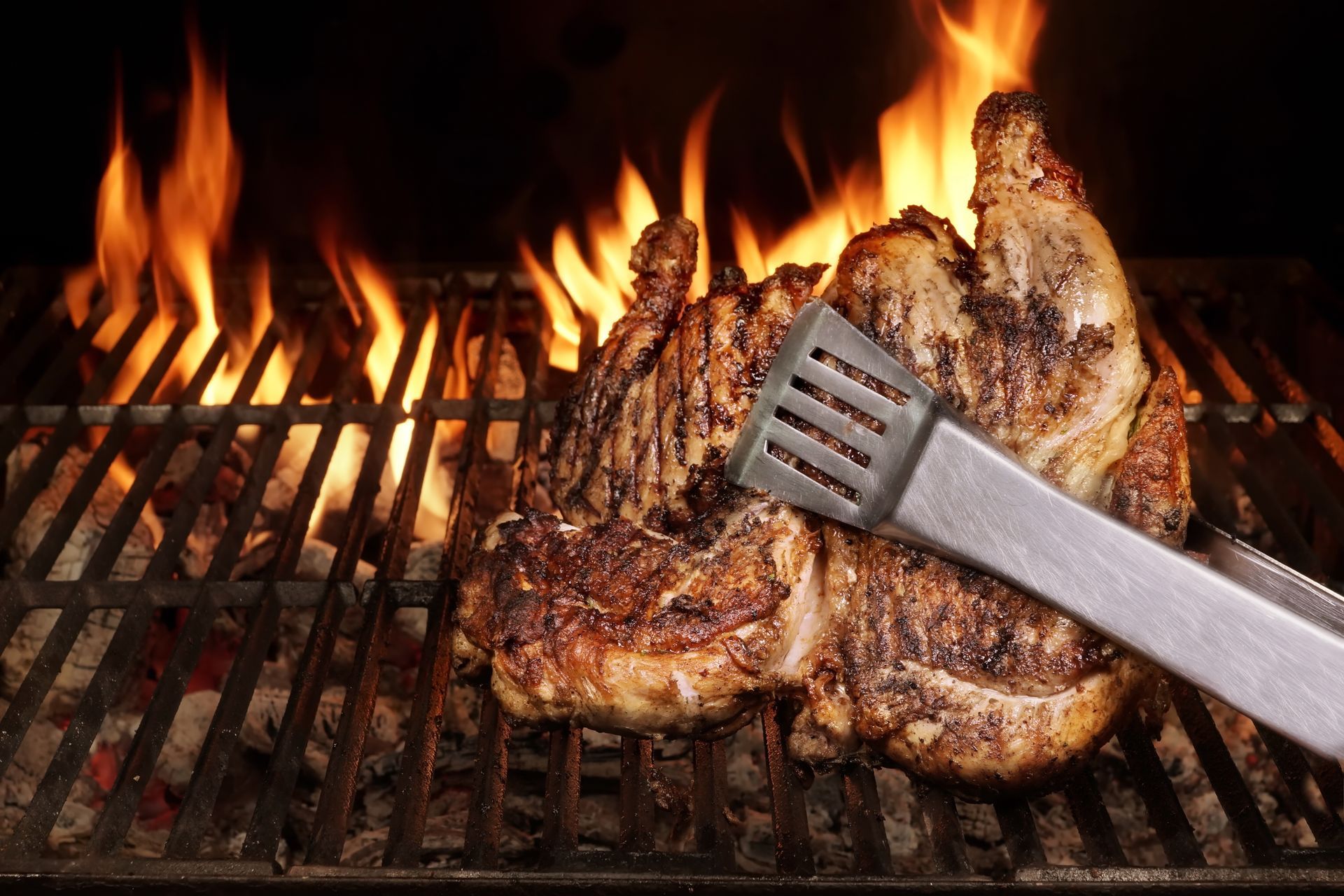 Steaks grilling over open flames on a barbecue, with a metal spatula lifting one piece.