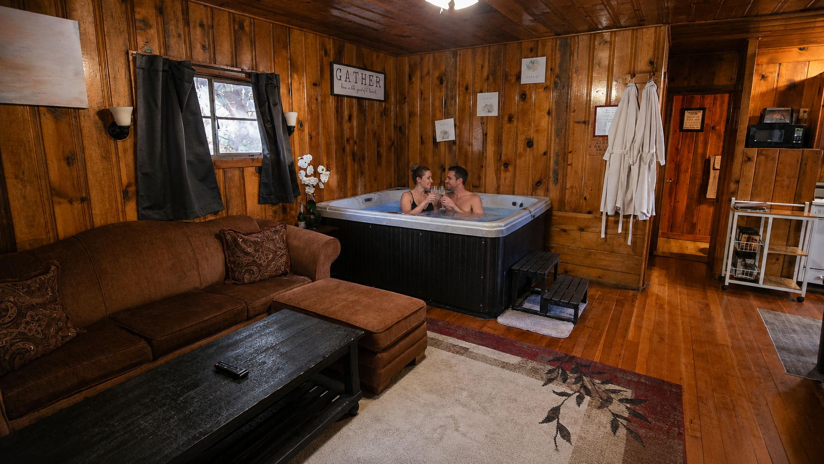 Rustic wood-paneled room with a brown couch, black hot tub, and beige rug under warm lighting