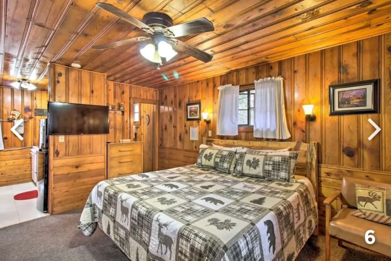 Cozy wood-paneled bedroom with a bed, ceiling fan, TV, and window curtains