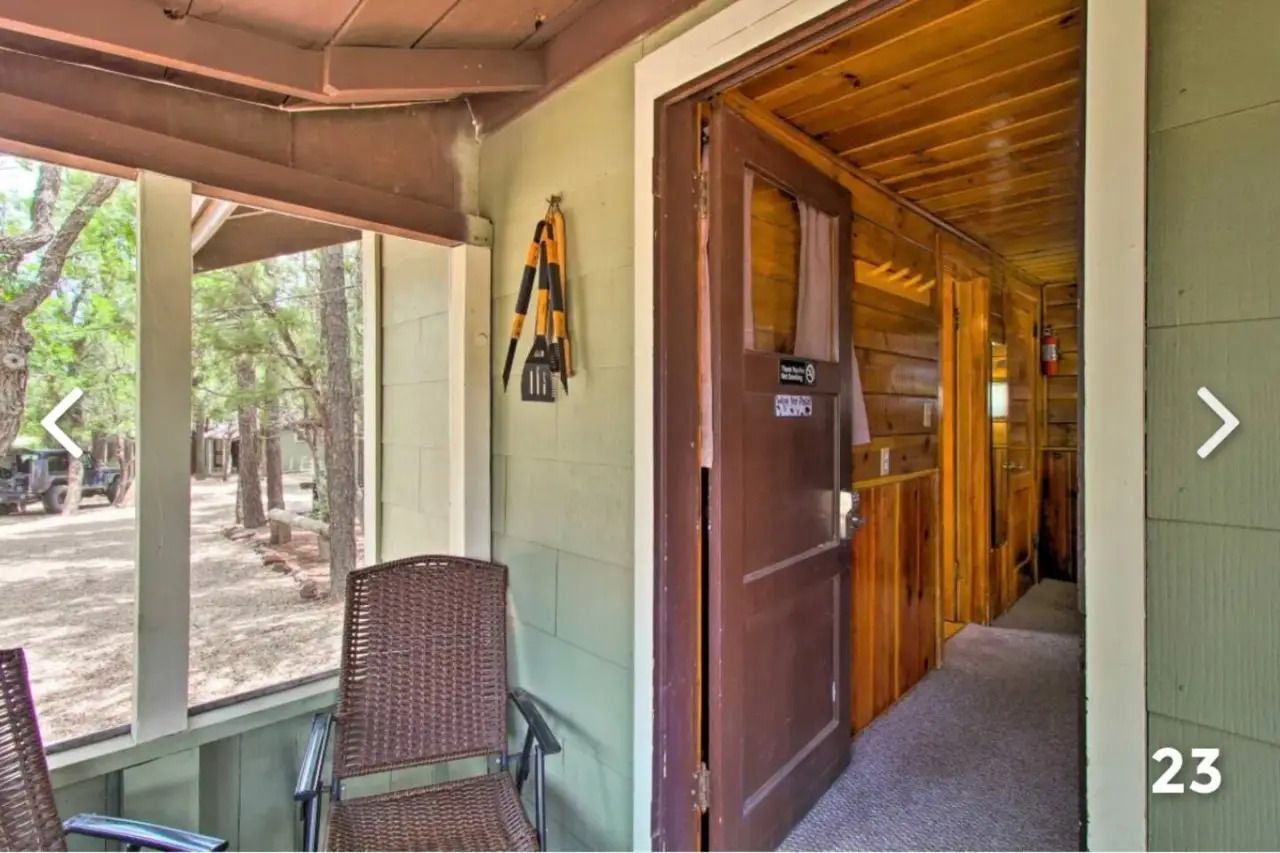 Porch entry with wicker chair, open wooden door, and view into a cabin hallway