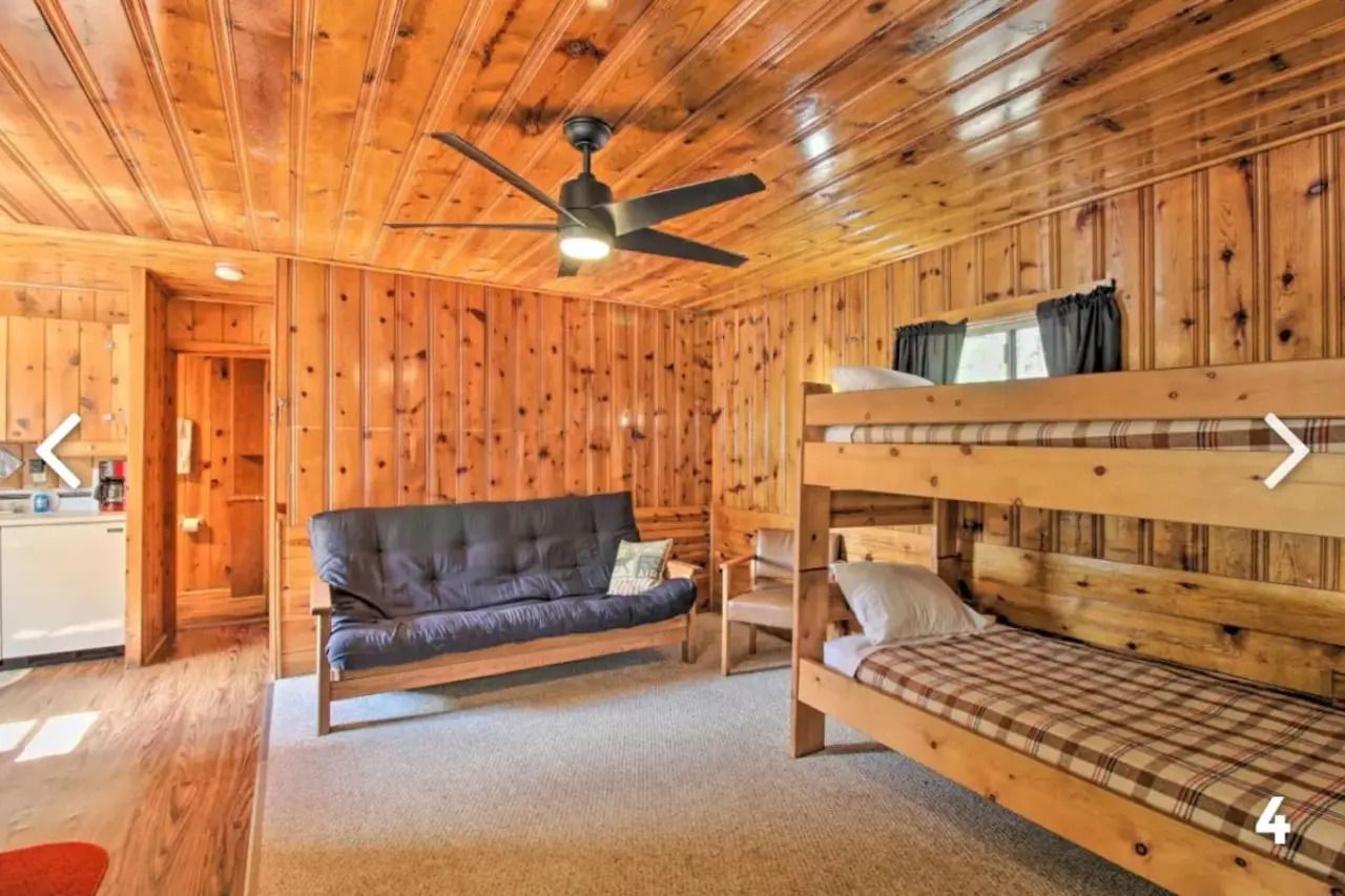 Wood-paneled cabin living room with futon, bunk bed, ceiling fan, and mirror.