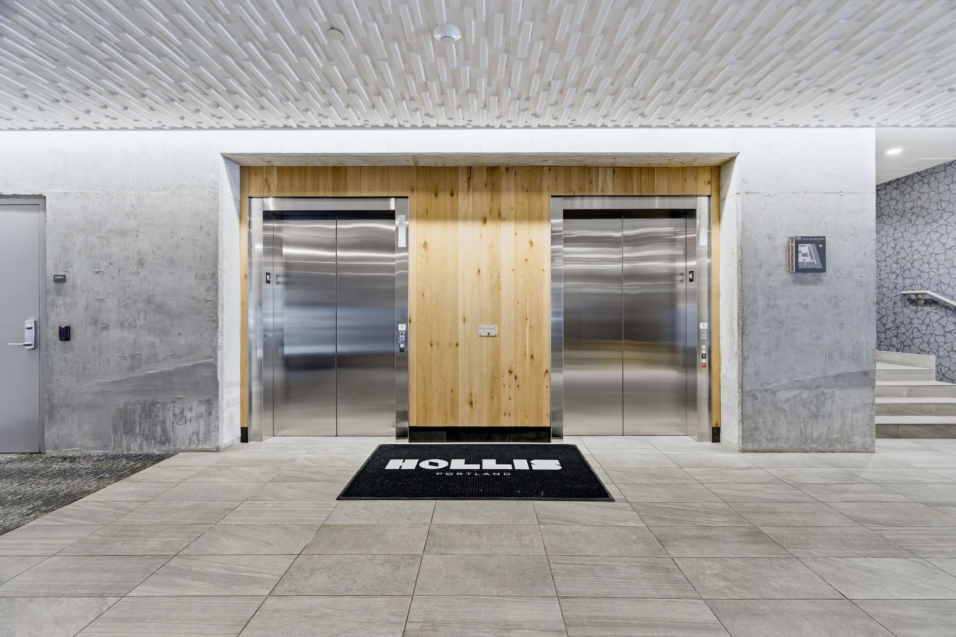 Modern lobby with two stainless steel elevators, wood-paneled center wall, and tiled floor