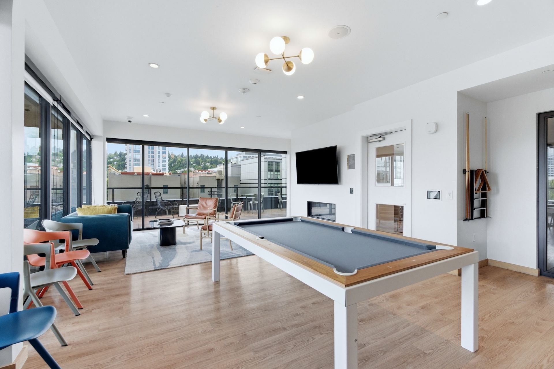 Bright game room with a pool table, seating area, wall TV, and large windows overlooking a city view