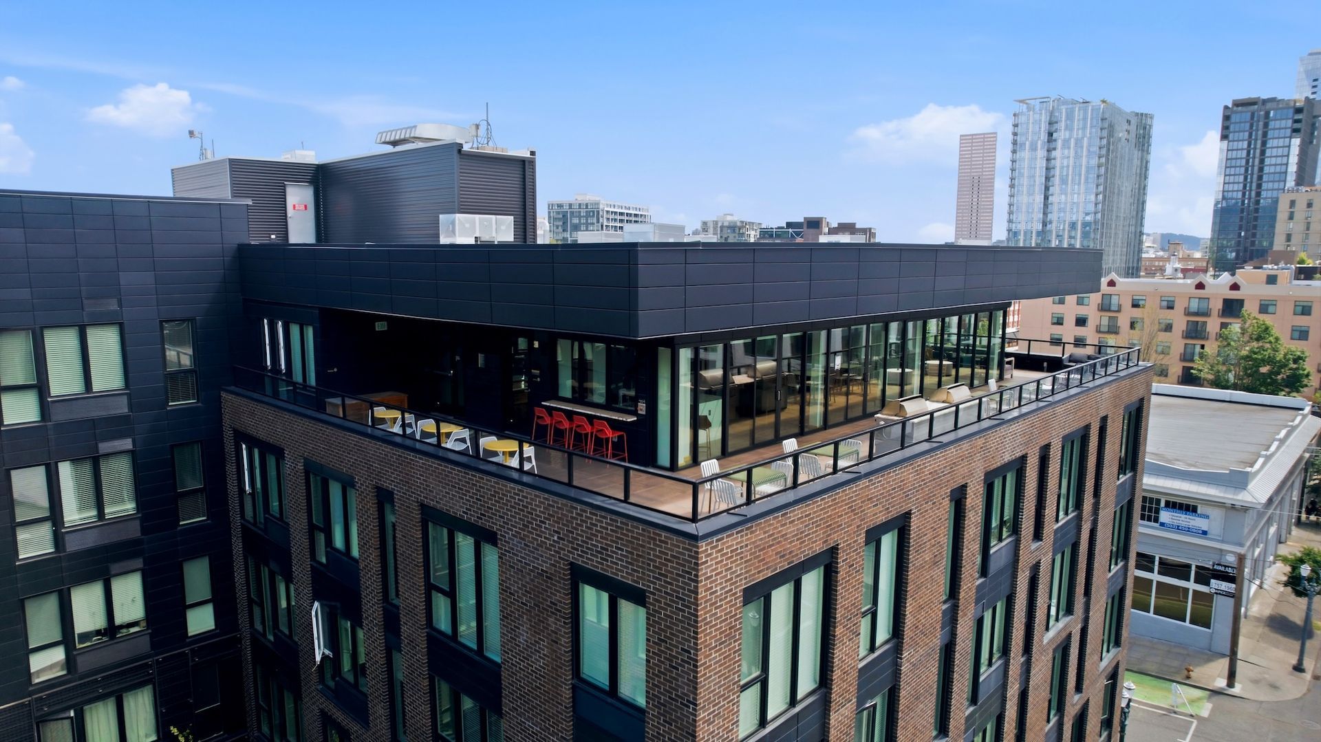 Rooftop view of a modern brick-and-glass building with a terrace, city skyline in the background