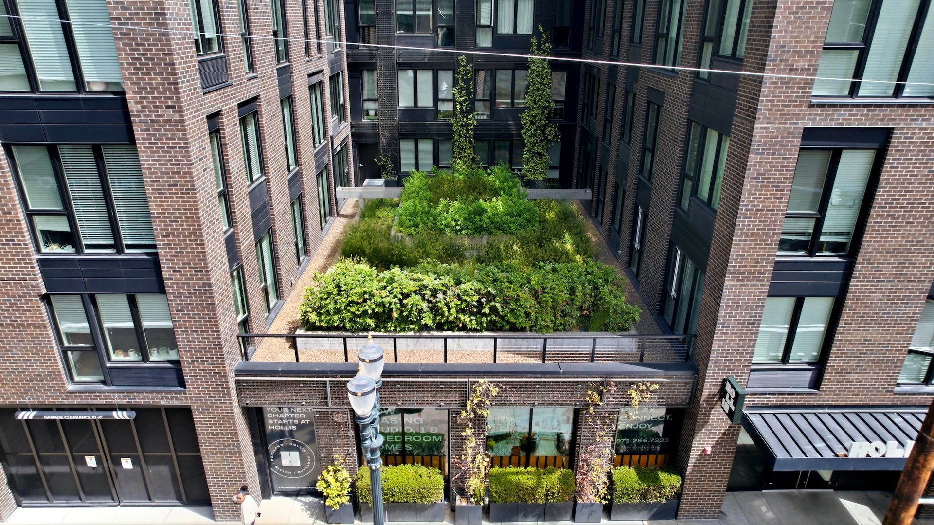 Courtyard between brick apartment buildings with a lush green rooftop terrace and glass entrance below