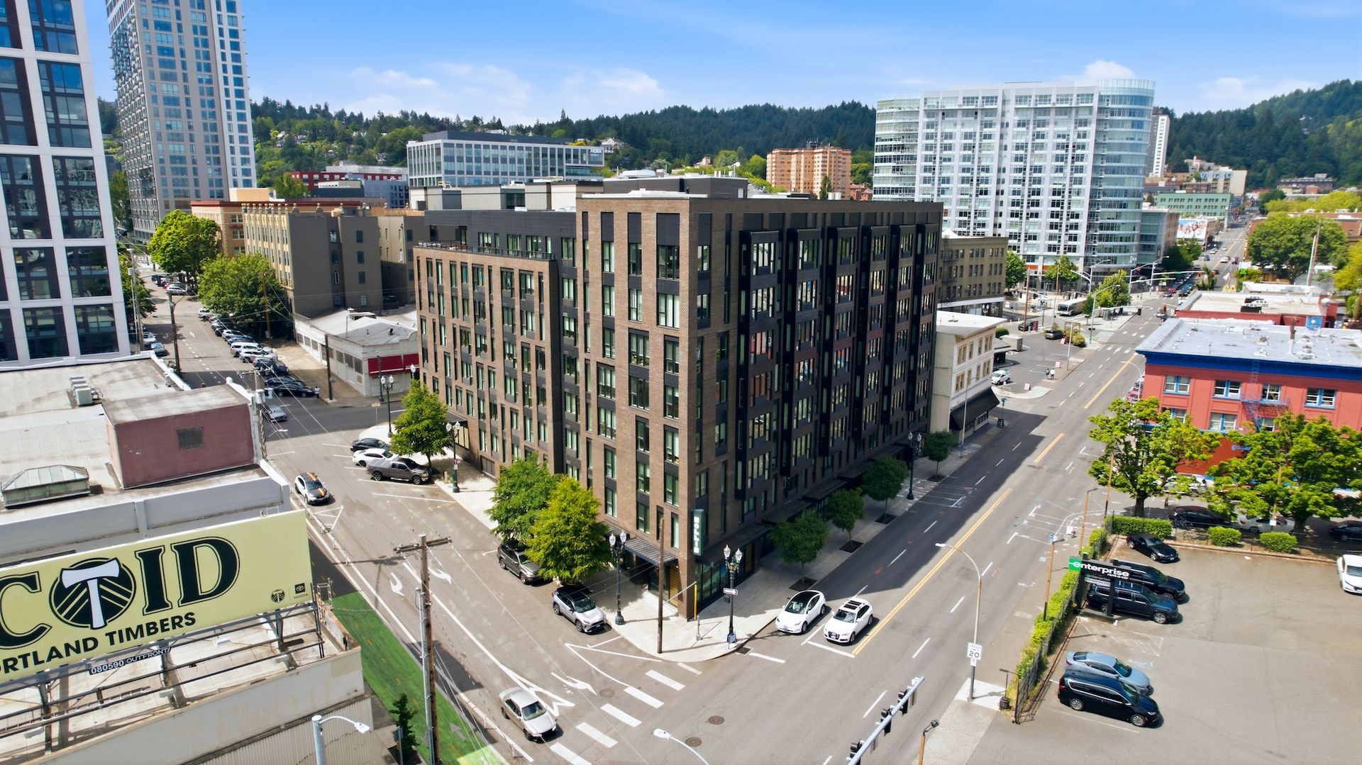 Aerial view of a city intersection with a large dark brick building and surrounding streets.