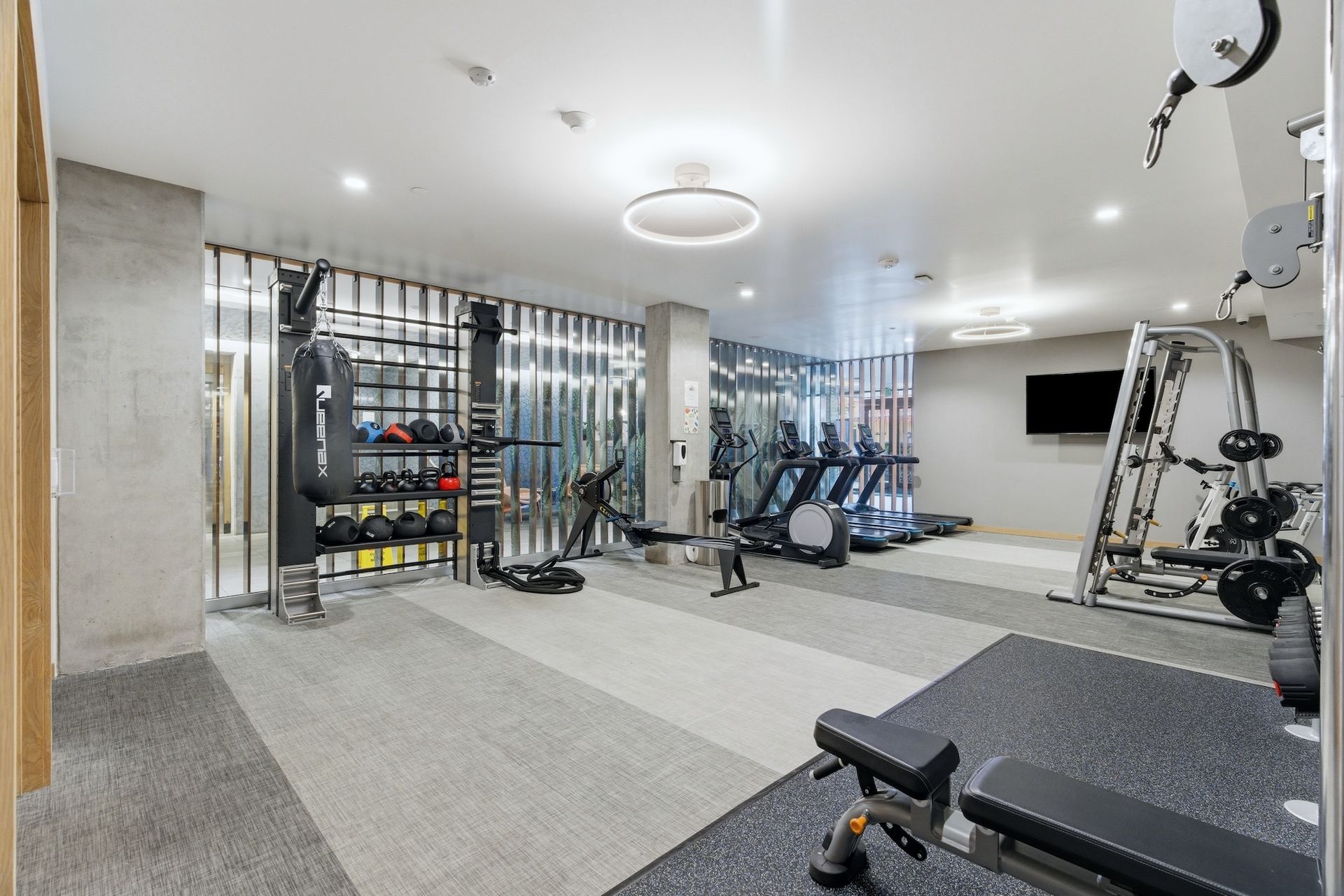 Modern gym with cardio machines, weights, and mirrors on a light gray floor