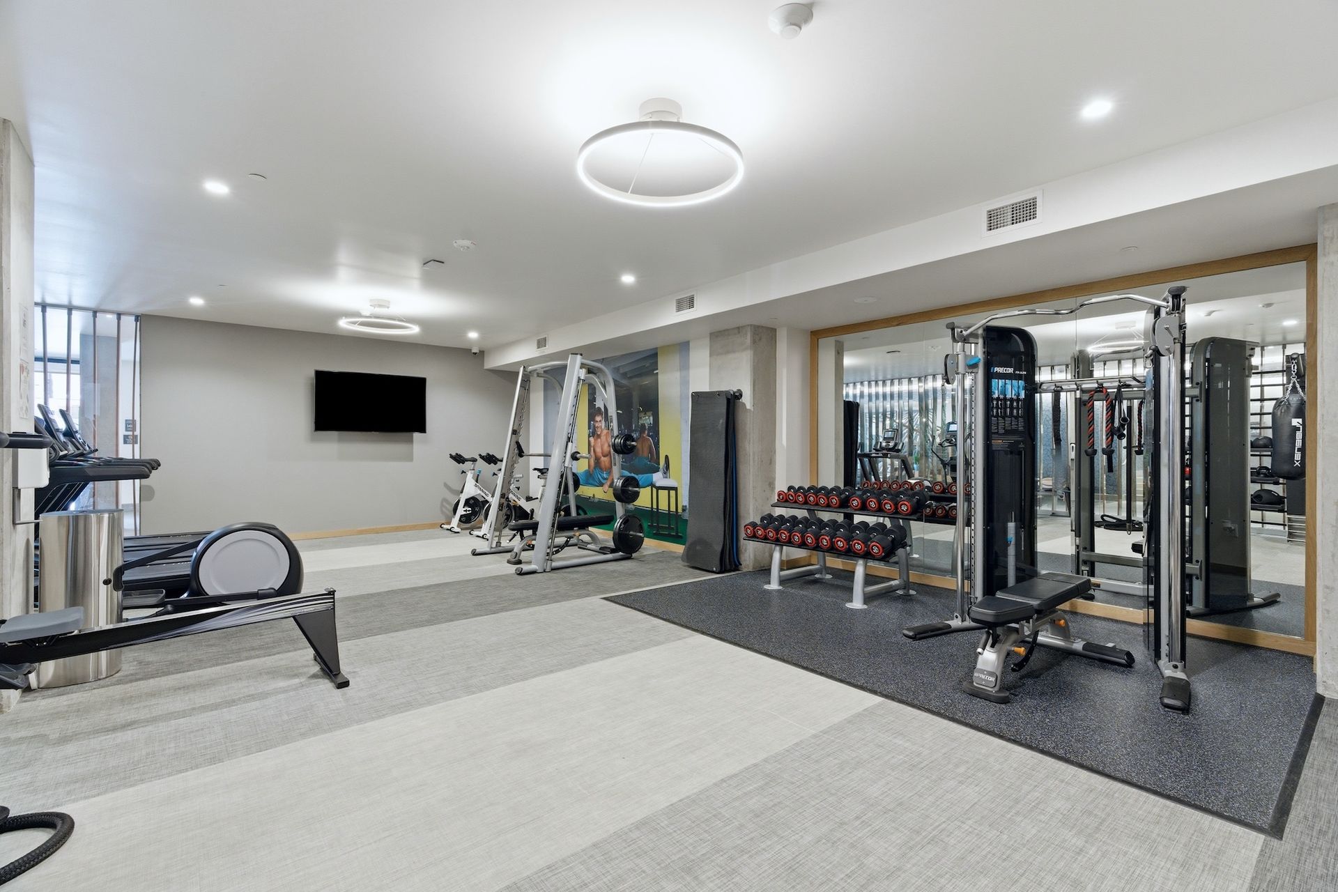 Modern gym interior with exercise machines, cable stations, and wall-mounted TV.