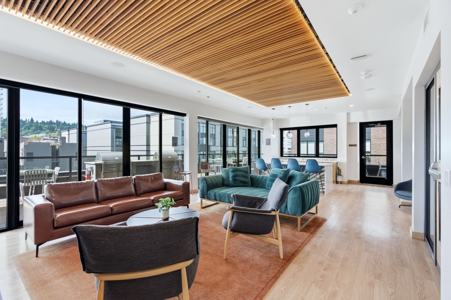 Modern living room with brown and teal sofas, wood ceiling, and large windows overlooking a city view