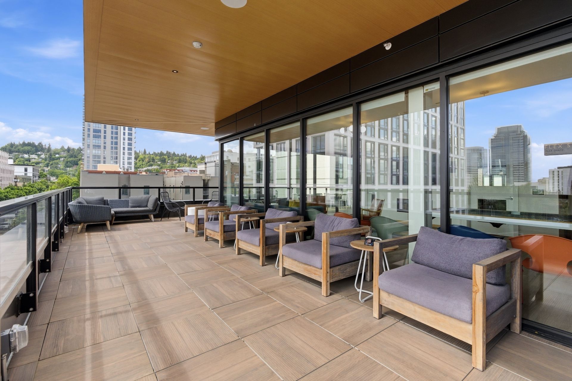 Spacious rooftop terrace with lounge chairs, wooden deck, glass railings, and city views