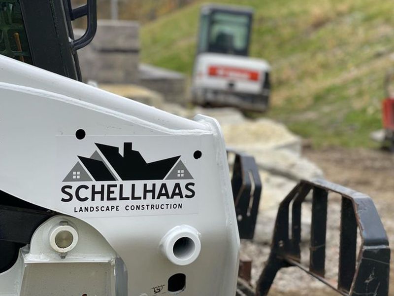 White Schellhaas construction machine in foreground with roadwork vehicle and dirt path in background