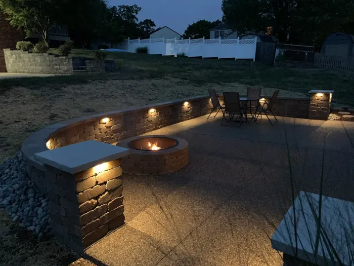 Lit stone patio seating area with curved retaining wall, built-in lights, and outdoor chairs at dusk