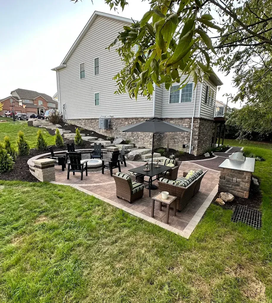 Backyard patio with outdoor dining set, umbrella, grill, and stone fire pit beside a house