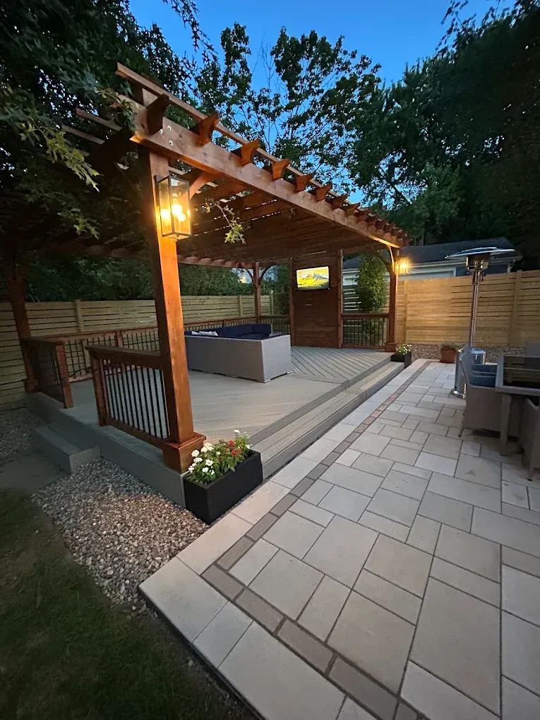 Backyard patio with pergola, warm lantern light, tiled seating area, and wooden privacy fencing at dusk