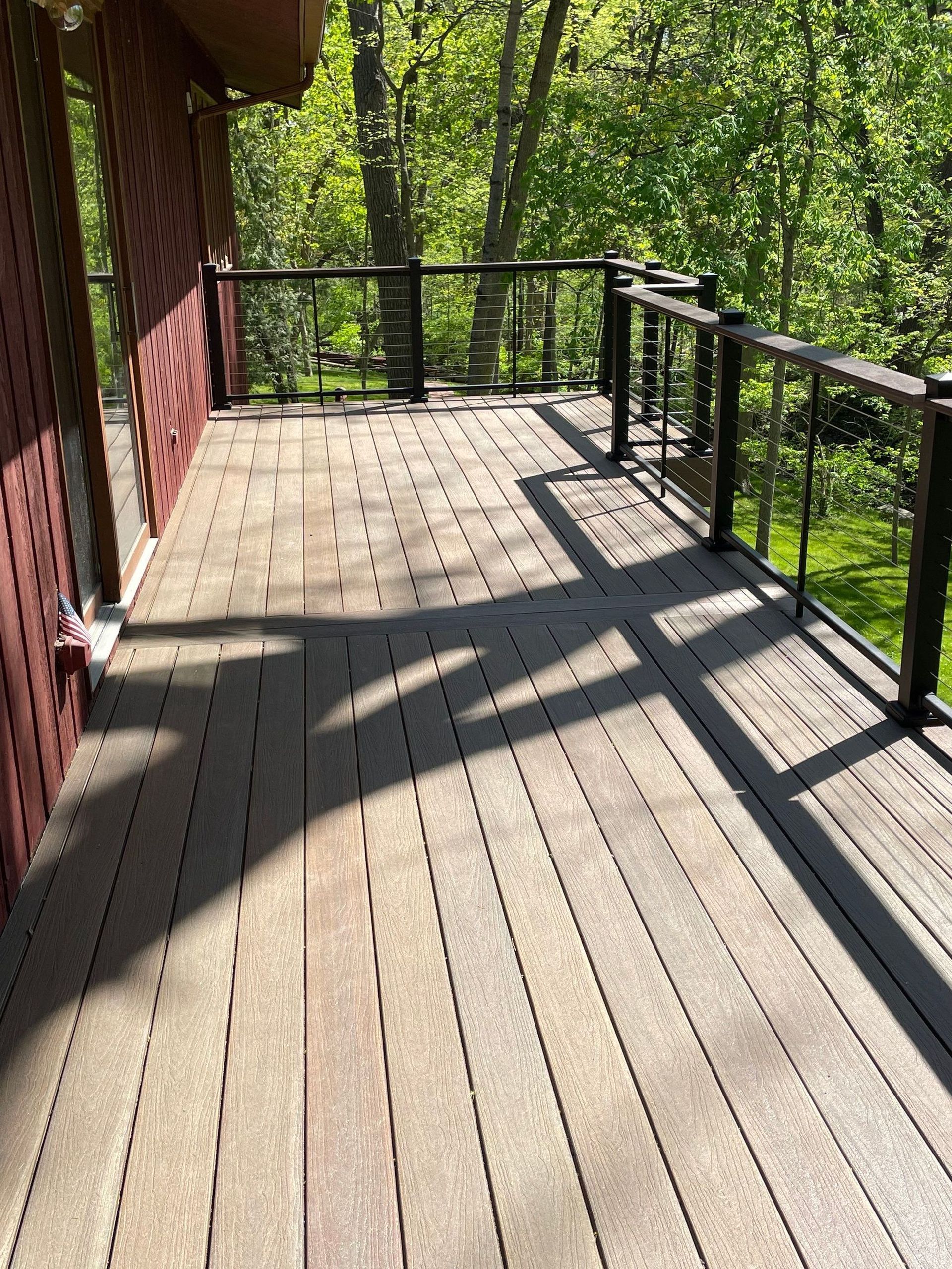 Deck with dark brown composite boards, black railing, and sunlight casting shadows.