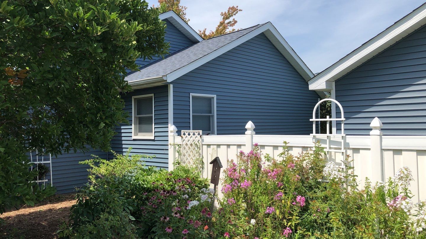 Blue house with white fence and green bushes; sunny day.