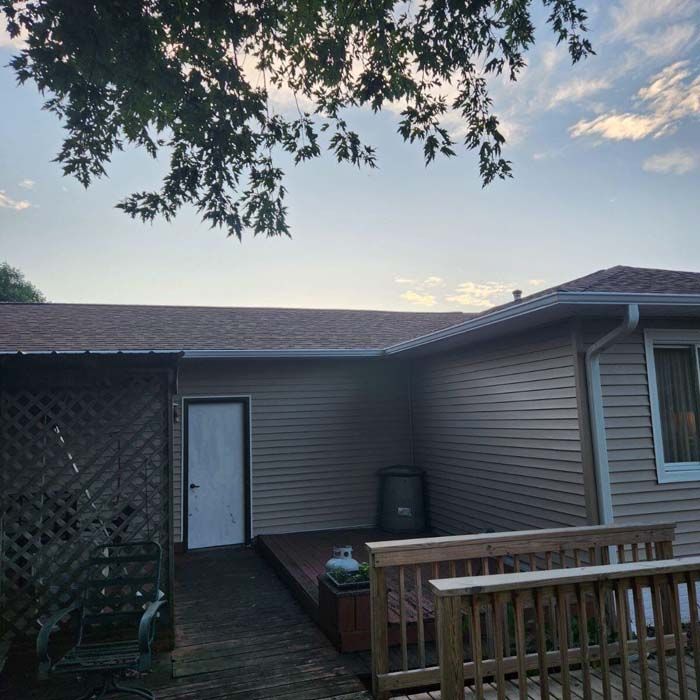 Backyard deck with brown siding house, dark roof, cloudy sky, and tree branches.