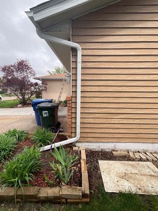 Tan siding with white gutter and downspout next to a green trash bin on a cloudy day.