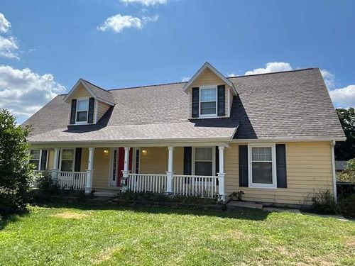 Yellow house with white porch, black shutters, and two dormers under a blue sky.