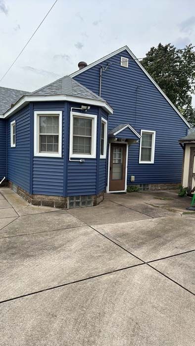 Back of a blue house with windows, a door, and a concrete patio.