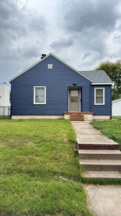 Blue house with white trim, gray roof, and a concrete path leading to the front door.