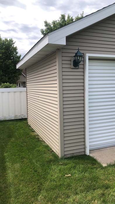 Tan garage with white trim and a green light, next to a grassy lawn and white fence.