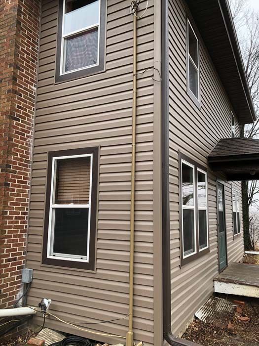 Two-story house with tan siding, brown trim, and a brick chimney.