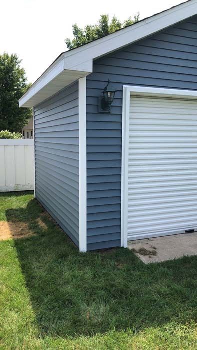Blue-sided garage with white trim, a closed white garage door, and a black light fixture.