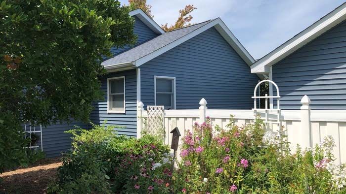 Blue house with white fence and flowering bushes.
