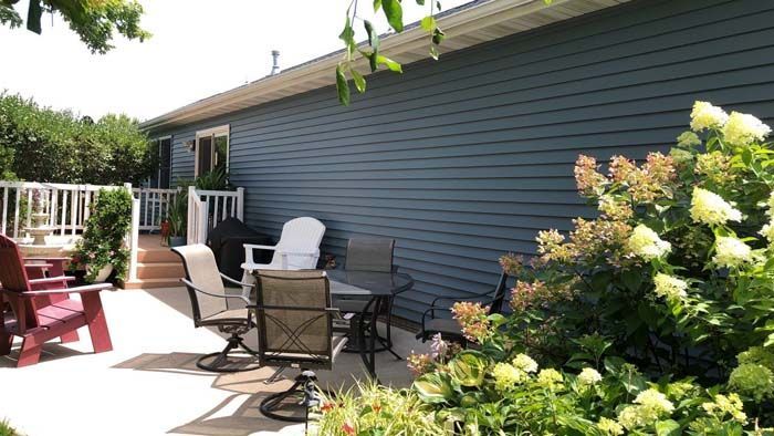 Patio with outdoor furniture next to a blue house and surrounded by greenery.