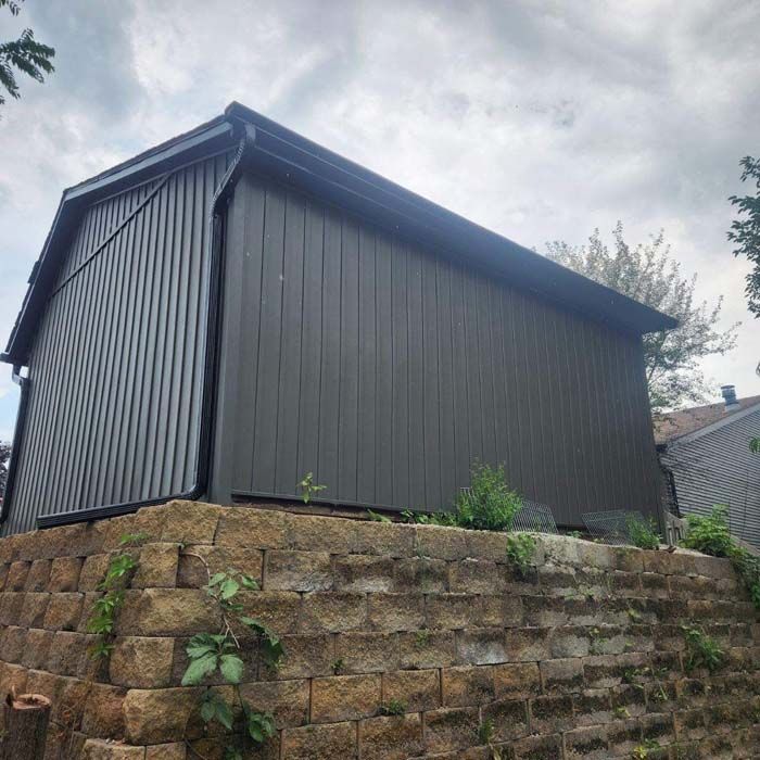 Dark gray shed on a stone retaining wall, under an overcast sky.