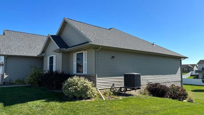 Tan house with gray roof, green lawn, blue sky. Air conditioning unit on side of house.