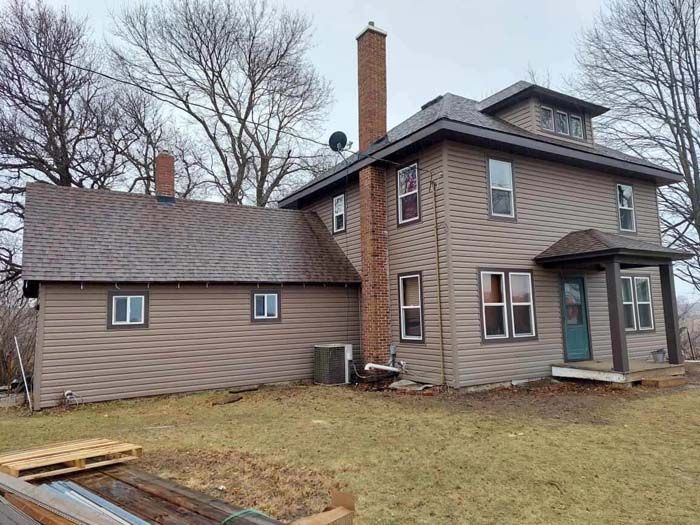 Two-story brown house with a chimney, siding, and a small porch. Overcast day.