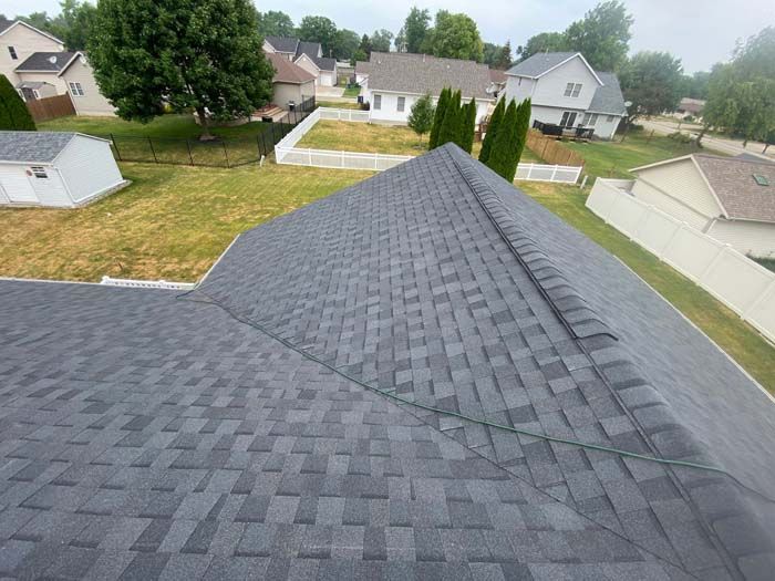 Gray asphalt shingle roof on a residential building, viewed from above, with surrounding yards and houses.