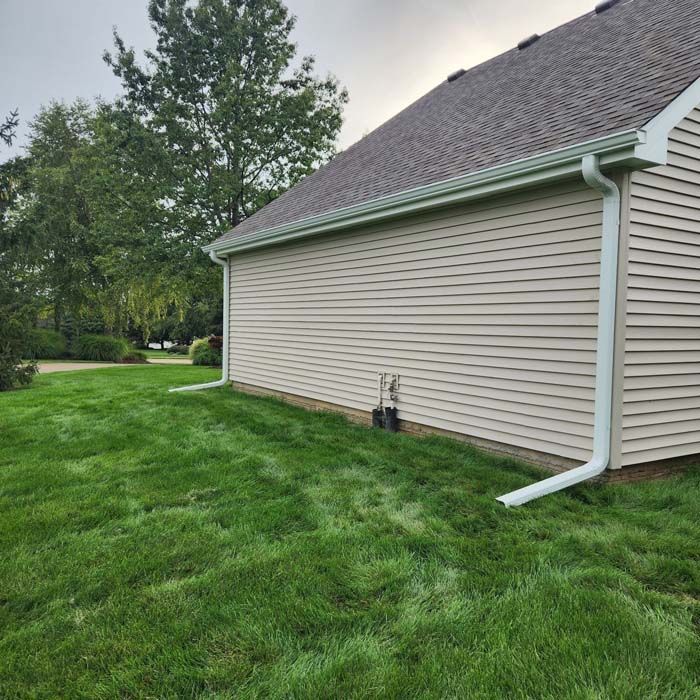 Side of a beige house with green lawn, white gutters, and downspout.