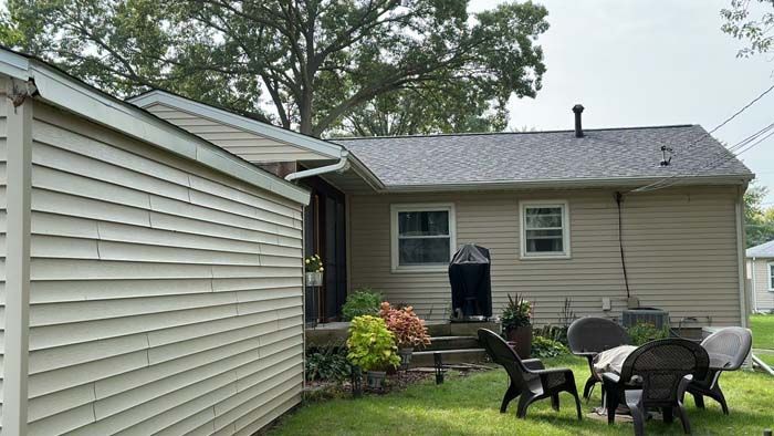 Backyard view of a beige house with a detached shed and patio furniture on the grass.