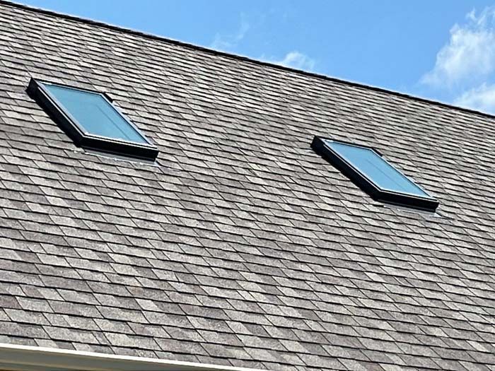 Two rectangular skylights in a gray shingle roof against a blue sky.