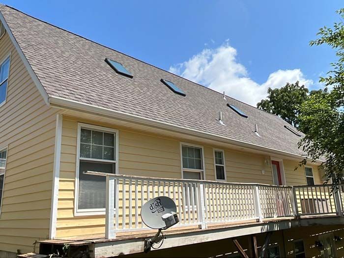 Yellow house with a brown roof and skylights, deck with railing, and a satellite dish.