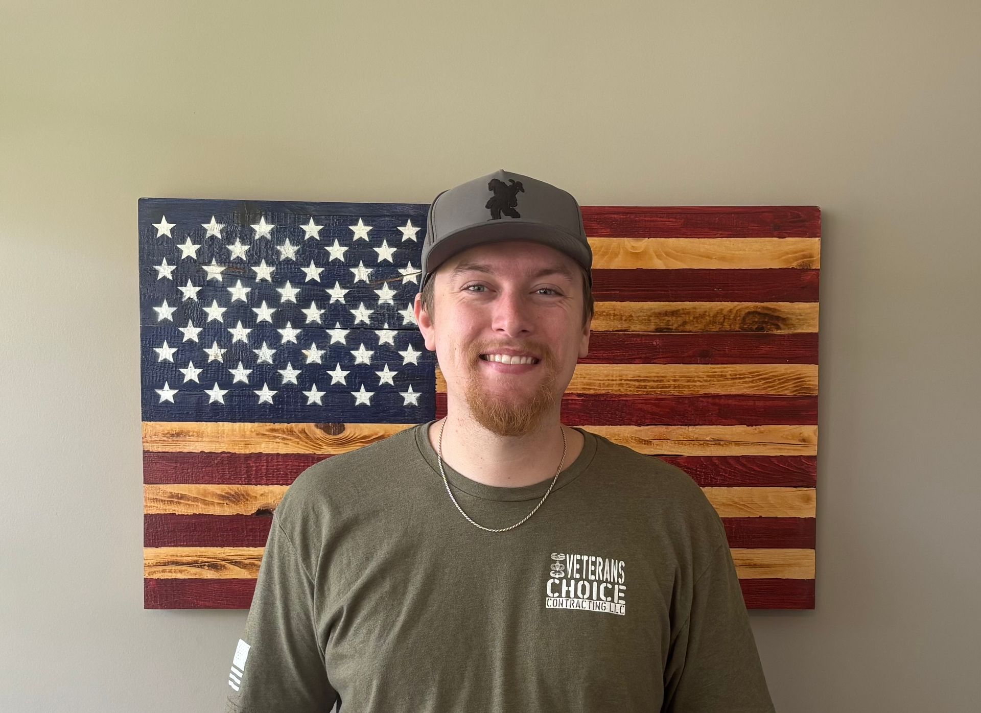 Man in black polo shirt stands in front of a wooden American flag.