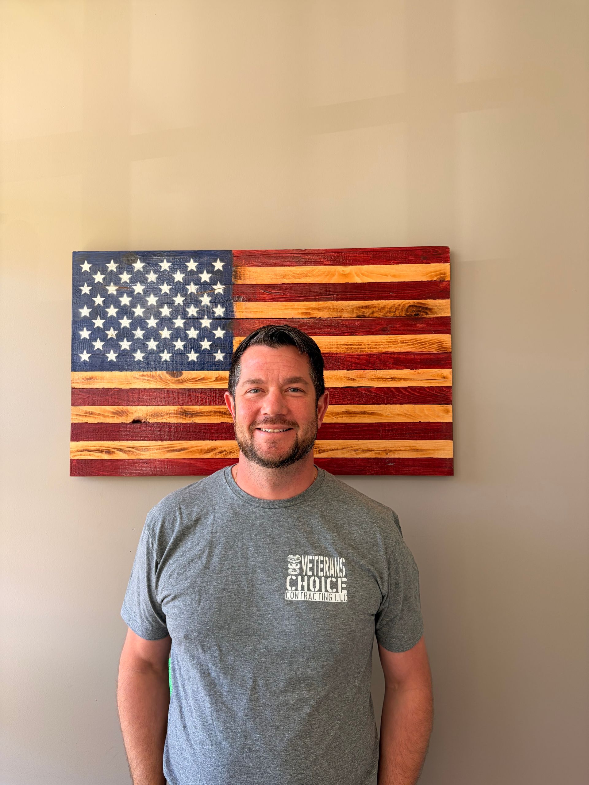 Man in black polo shirt stands in front of a wooden American flag.