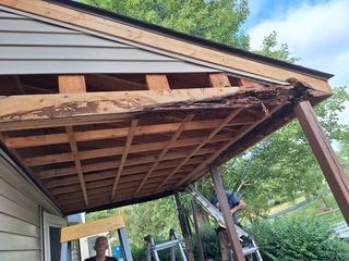 Damaged carport roof with exposed beams and sagging panels beside a house