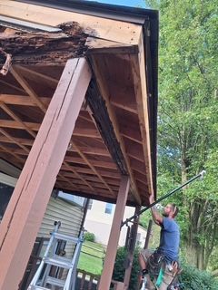 Worker using a long pole to inspect or repair the underside of a wooden porch roof outdoors